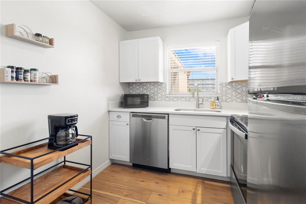 A kitchen features white cabinets, stainless steel appliances, a patterned backsplash, and wood-look flooring — 4480 IRONWOOD CIRCLE UNIT 309A, BRADENTON, FL