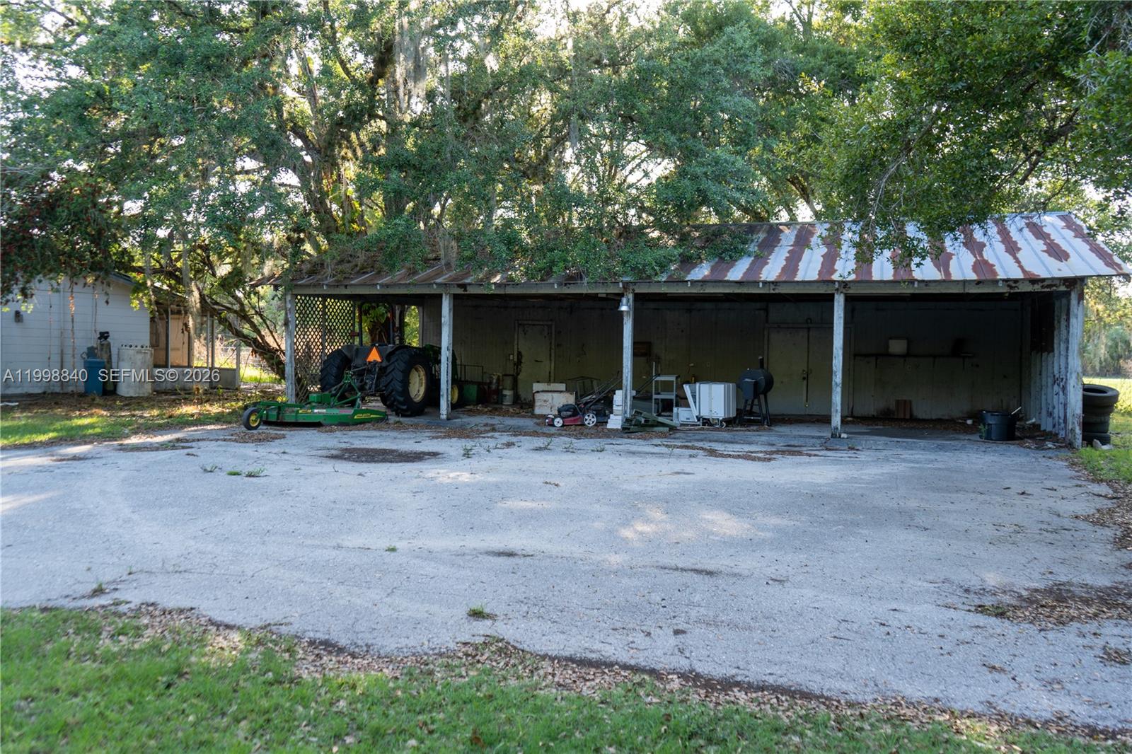 A large, open-sided metal shed with a rusted roof sits on a concrete pad — 120 CR 78, La Belle FL 33935, LA BELLE, FL