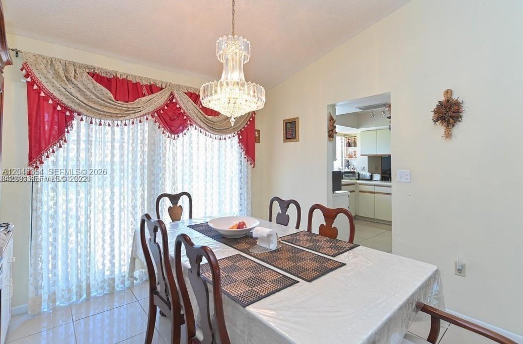 A dining room features a crystal chandelier, a table with place settings, and window curtains — 9612 SW 117th Ave # 9612, Miami FL 33186, MIAMI, FL