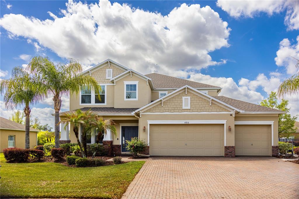 A two-story suburban house features a tan stucco exterior, a brick driveway, and palm trees — 4810 LAKE MILLY DRIVE, ORLANDO, FL