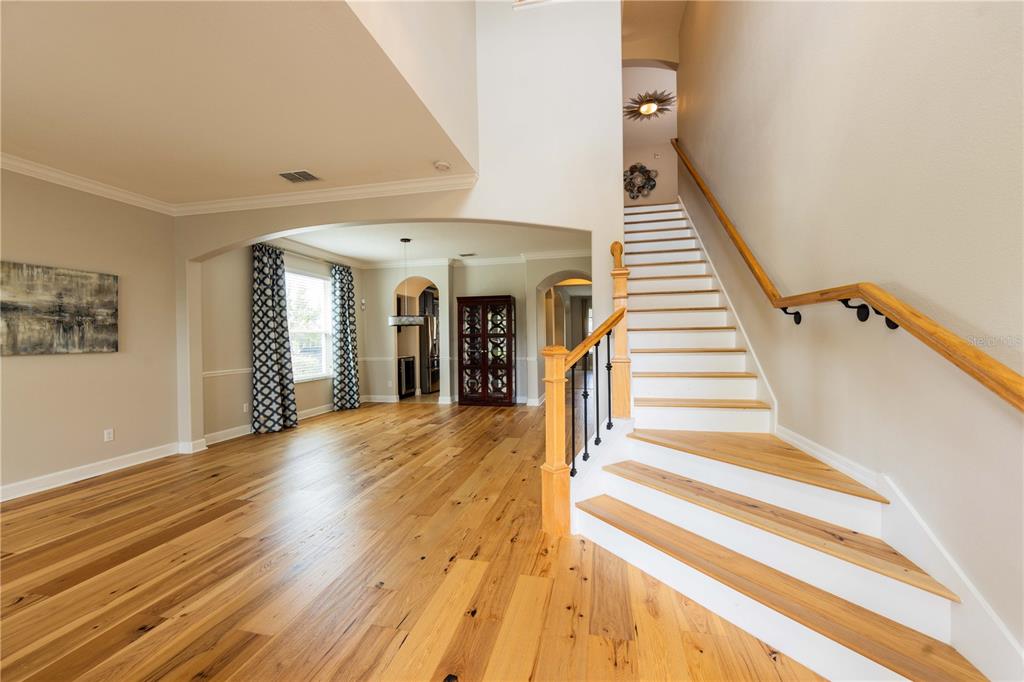 A bright foyer features hardwood floors, a staircase with a wooden railing, and arched doorways — 4810 LAKE MILLY DRIVE, ORLANDO, FL