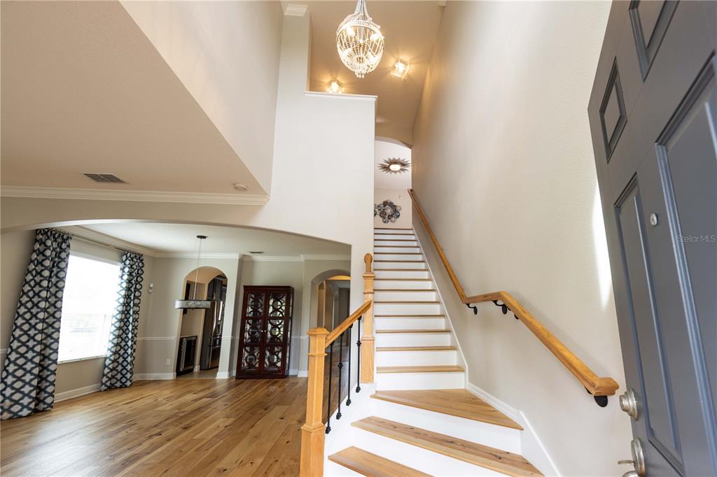 An entryway features a wooden staircase, a crystal chandelier, and an arched opening to a room — 4810 LAKE MILLY DRIVE, ORLANDO, FL