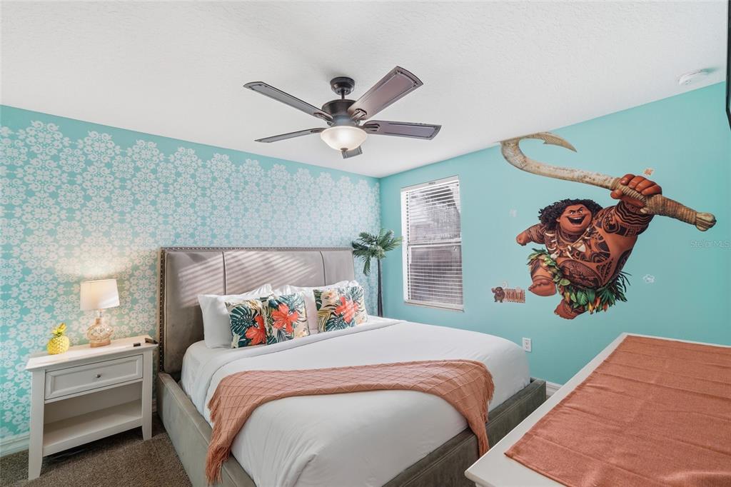 A bedroom features a bed with a gray headboard, patterned wallpaper, and a Maui wall decal — 1414 THUNDERBIRD ROAD, DAVENPORT, FL