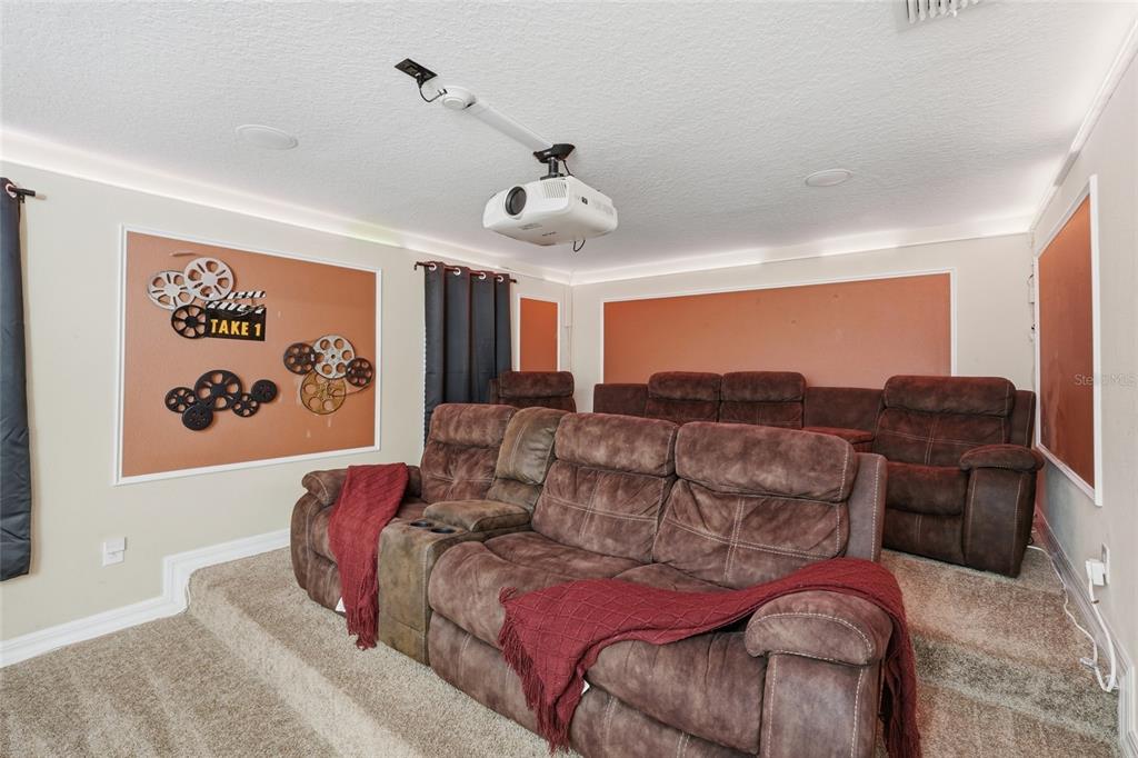 A home theater room features tiered seating with brown recliners, a ceiling-mounted projector, and wall decor — 1414 THUNDERBIRD ROAD, DAVENPORT, FL