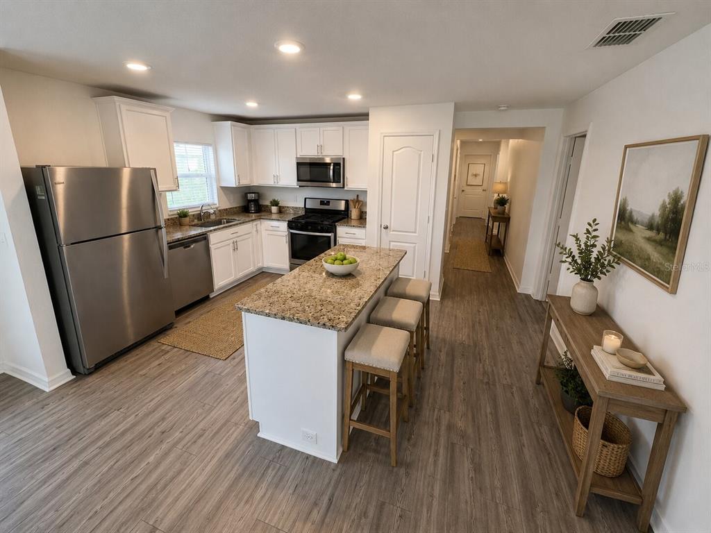 A kitchen features white cabinets, granite countertops, a center island with stools, and stainless appliances — 233 KENSINGTON VIEW BOULEVARD, WINTER HAVEN, FL