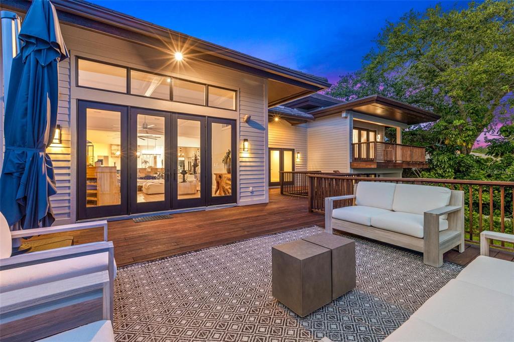 A wooden deck features outdoor furniture and a patterned rug outside a house with glass doors — 1365 BRIGHTWATERS BOULEVARD NE, ST PETERSBURG, FL