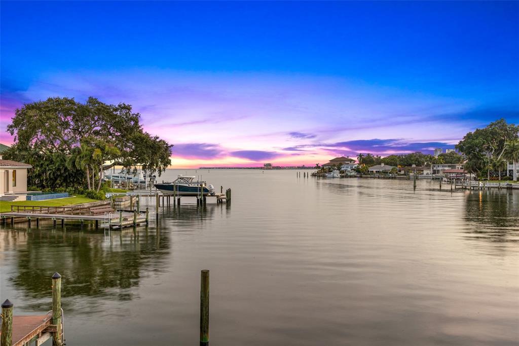 A calm waterfront view at sunset featuring a wooden dock, a boat, and nearby houses — 1365 BRIGHTWATERS BOULEVARD NE, ST PETERSBURG, FL