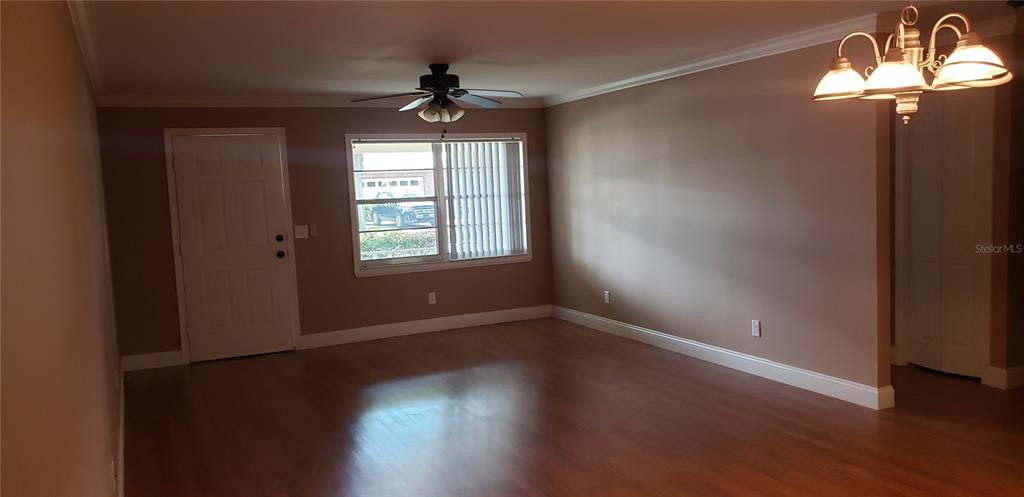 An empty living room features wood-look flooring, a ceiling fan, and a chandelier — 9142 SW 82ND TERRACE UNIT C, OCALA, FL