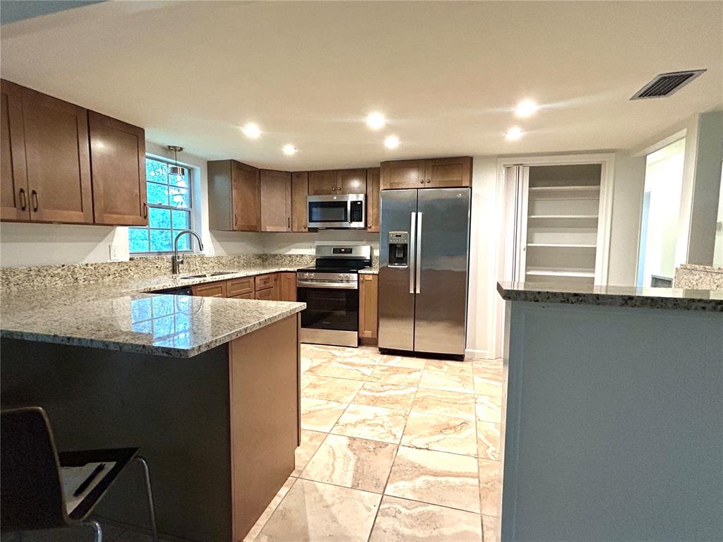 A kitchen features wood cabinets, granite countertops, stainless steel appliances, and light-colored tile flooring — 7532 SW 122ND STREET, GAINESVILLE, FL