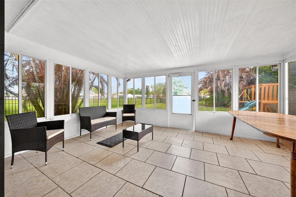 A sunroom features tiled floors, white paneled ceilings, wicker furniture, and large windows overlooking a yard — 5107 DEER CREEK DRIVE, ORLANDO, FL