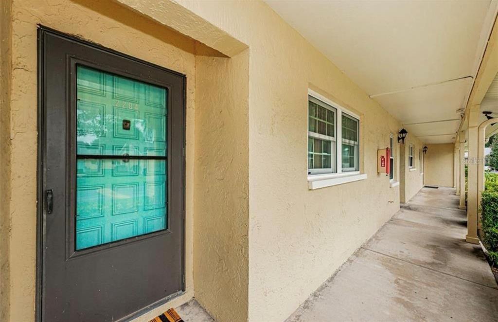 A beige exterior wall features a dark-framed door and a window along a concrete walkway — 2465 NORTHSIDE DRIVE UNIT 2204, CLEARWATER, FL