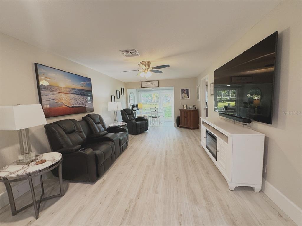 A living room features light wood-look flooring, a black leather sofa, and a wall-mounted television — 2465 NORTHSIDE DRIVE UNIT 2204, CLEARWATER, FL