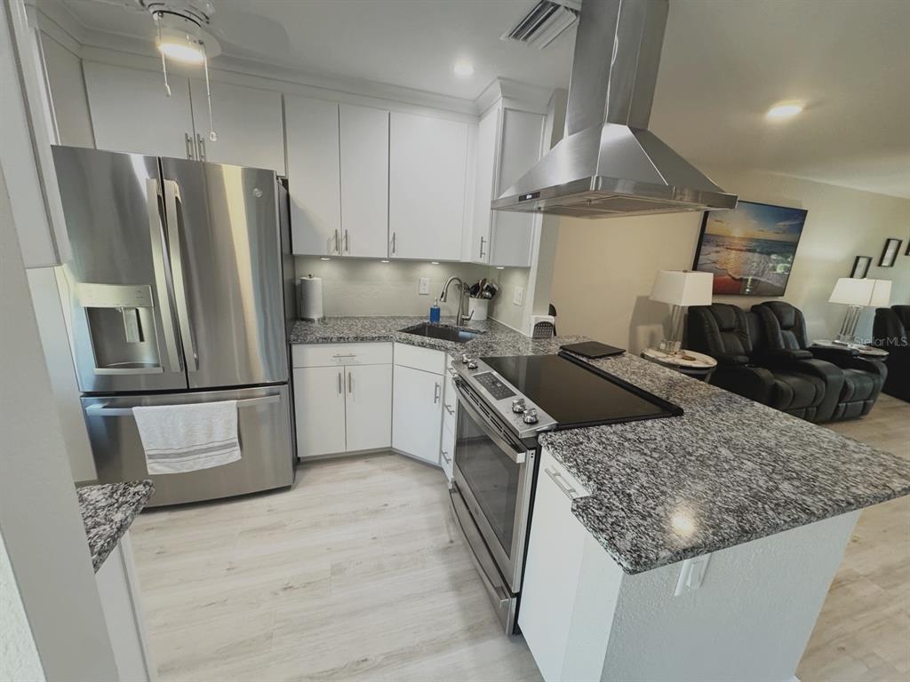 A kitchen features white cabinets, granite countertops, stainless steel appliances, and light wood-look flooring — 2465 NORTHSIDE DRIVE UNIT 2204, CLEARWATER, FL