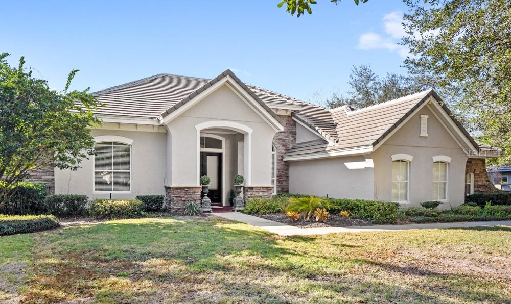 A single-story house with a beige stucco exterior, stone accents, and a tiled roof — 25515 HAWKS RUN LANE, SORRENTO, FL