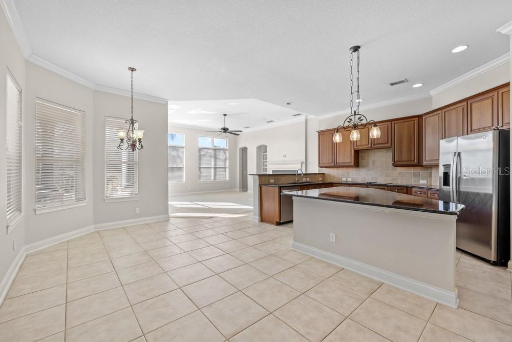 A kitchen with wooden cabinets, a granite island, and tile flooring opens to a dining area — 25515 HAWKS RUN LANE, SORRENTO, FL