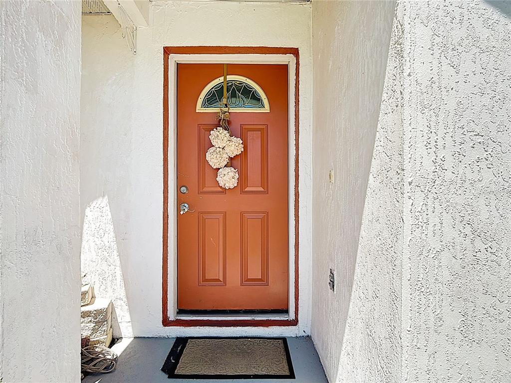 An orange front door with a decorative wreath sits in a white stucco entryway — 852 FRANCONVILLE COURT, KISSIMMEE, FL