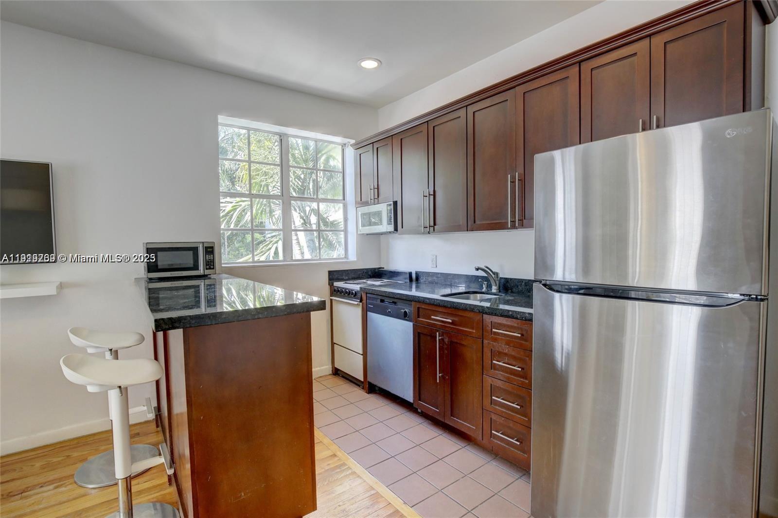 A kitchen features dark wood cabinets, stainless steel appliances, a granite countertop, and two stools — 1127 Euclid Ave # 206, Miami Beach FL 33139, MIAMI BEACH, FL