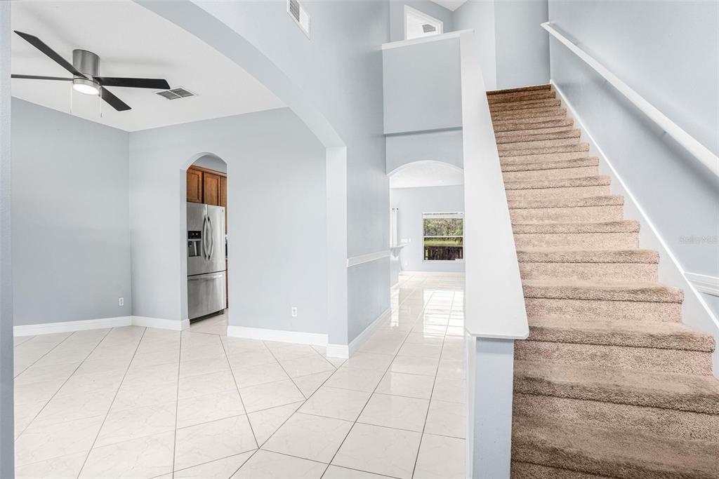 A carpeted staircase leads to an upper level next to a tiled room with a ceiling fan — 1892 HAMMOCK MOSS DRIVE, ORLANDO, FL
