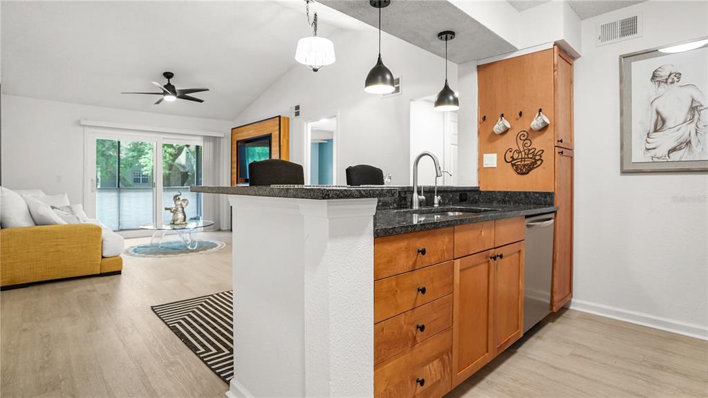 A kitchen with wood cabinets and granite countertops overlooks a living area with sliding doors — 2500 WINDING CREEK BOULEVARD UNIT I205, CLEARWATER, FL