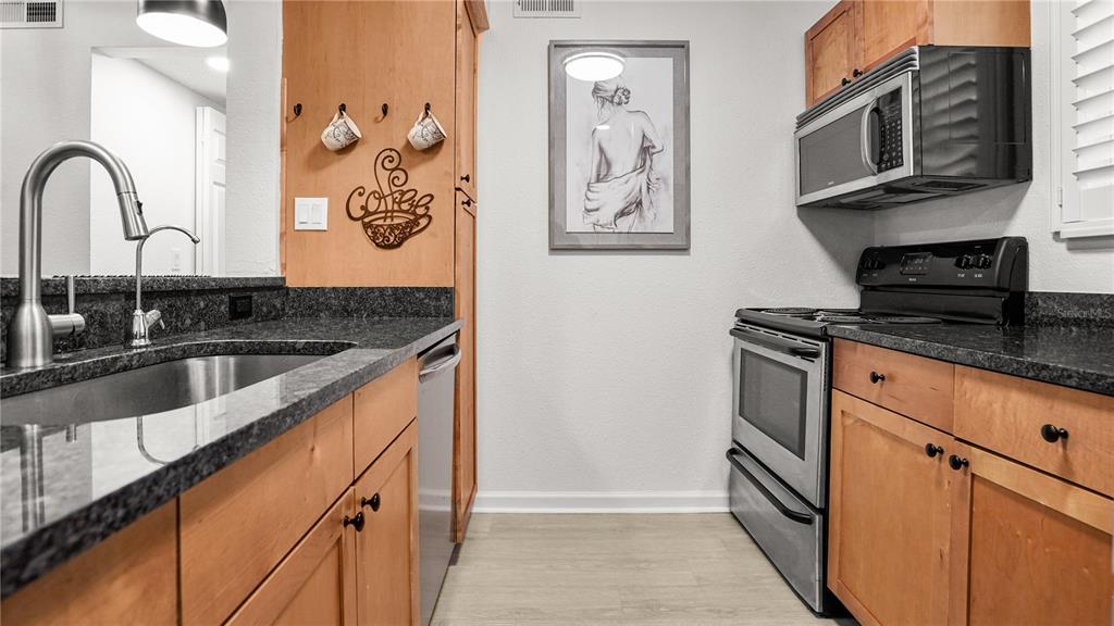 A kitchen features light wood cabinets, dark granite countertops, stainless steel appliances, and wall art — 2500 WINDING CREEK BOULEVARD UNIT I205, CLEARWATER, FL