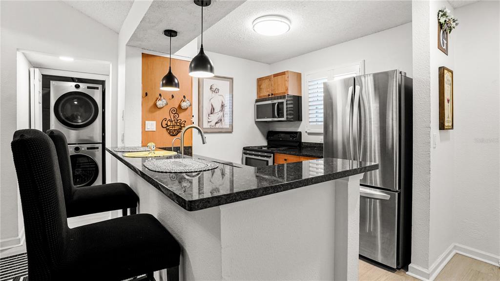 A kitchen features a breakfast bar with black countertops, stainless steel appliances, and stacked laundry units — 2500 WINDING CREEK BOULEVARD UNIT I205, CLEARWATER, FL