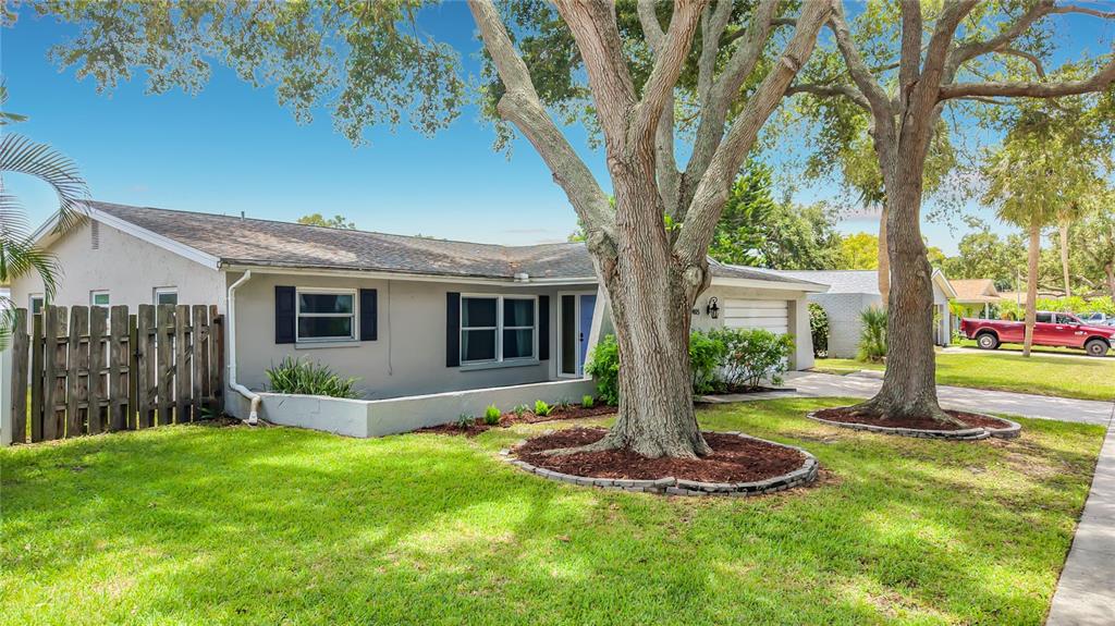A single-story house with a white exterior, a two-car garage, and two large front trees — 1405 OVERCASH DRIVE, DUNEDIN, FL
