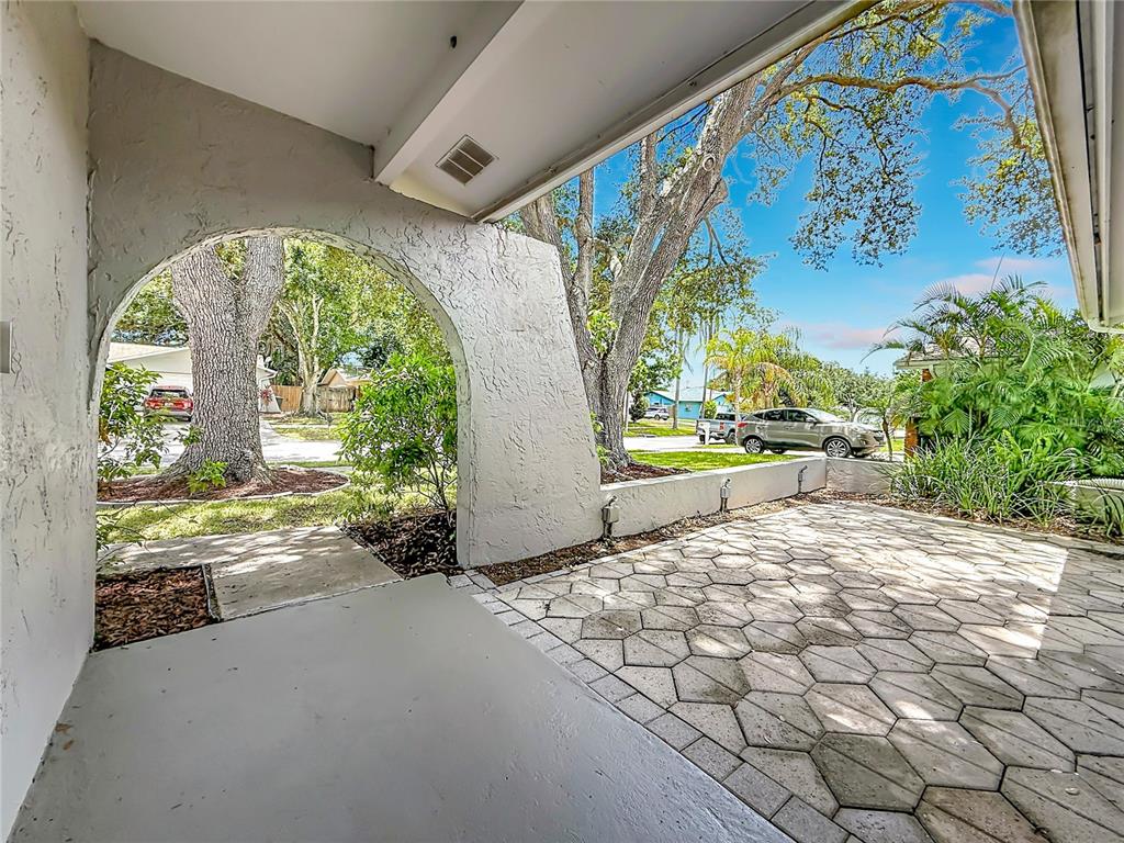 A covered patio with a stone-paved floor features a large arched opening overlooking a yard — 1405 OVERCASH DRIVE, DUNEDIN, FL