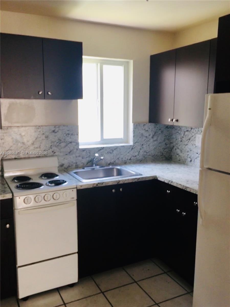 A kitchen features dark cabinets, white marble-patterned countertops, a white stove, and a window — 960 Biarritz Dr # 2, Miami Beach FL 33141, MIAMI BEACH, FL