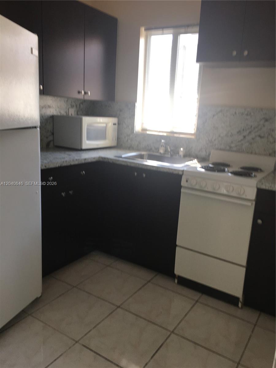 A small kitchen features dark cabinets, white appliances, and a window above the sink — 960 Biarritz Dr # 2, Miami Beach FL 33141, MIAMI BEACH, FL