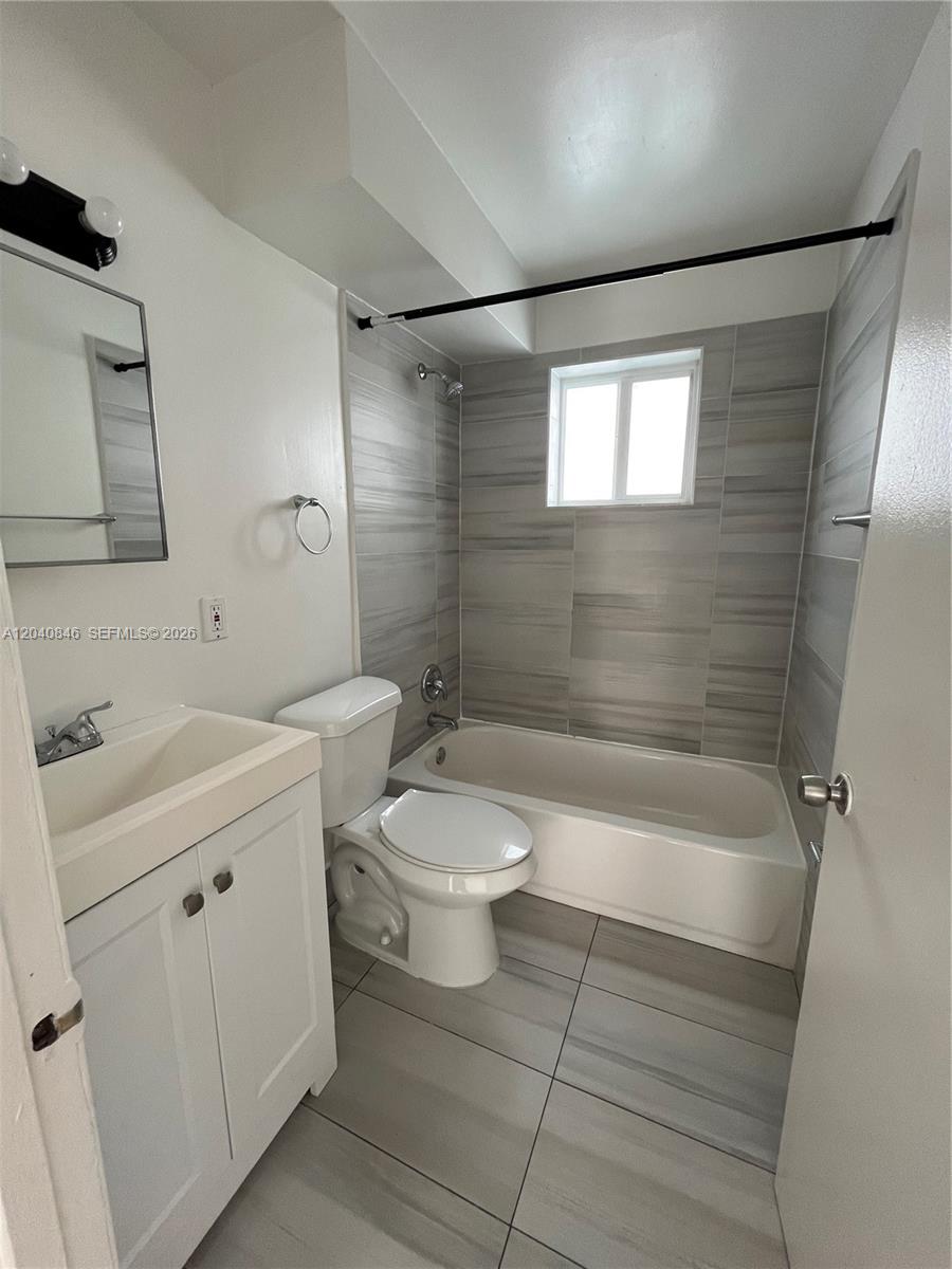 A bathroom features a white vanity, a toilet, and a bathtub with gray tiled walls — 960 Biarritz Dr # 2, Miami Beach FL 33141, MIAMI BEACH, FL