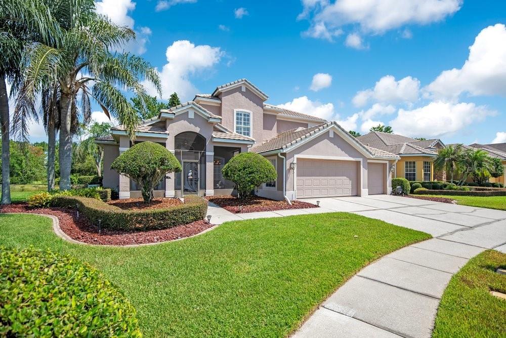 A two-story suburban house with a tan stucco exterior, a three-car garage, and landscaped lawn — 9211 SHADOW PINAR COURT, ORLANDO, FL