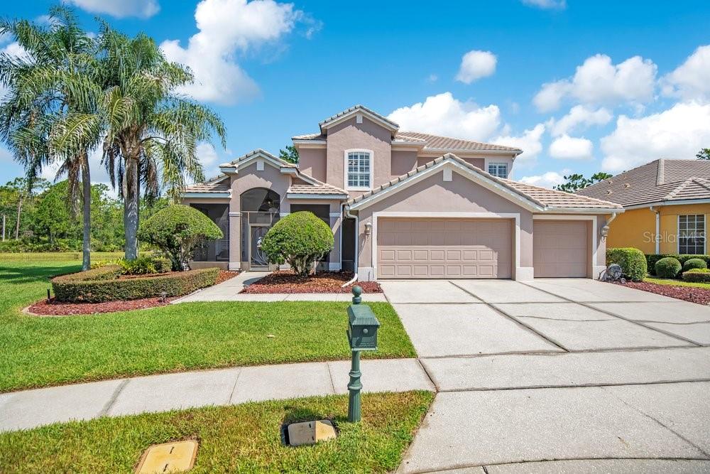 A two-story suburban house with a tan stucco exterior, a three-car garage, and landscaping — 9211 SHADOW PINAR COURT, ORLANDO, FL