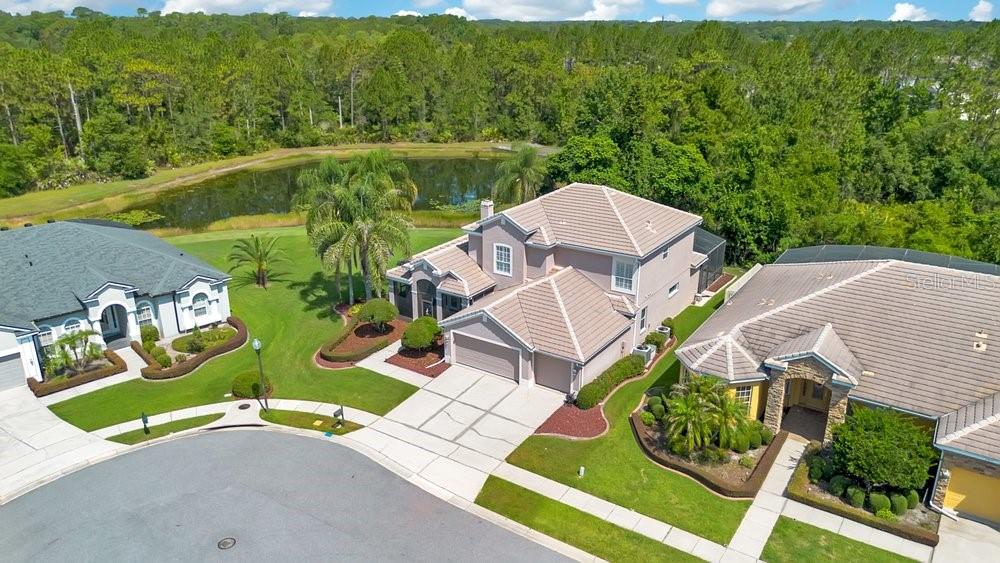 An aerial view of three suburban houses with tile roofs situated near a small pond — 9211 SHADOW PINAR COURT, ORLANDO, FL