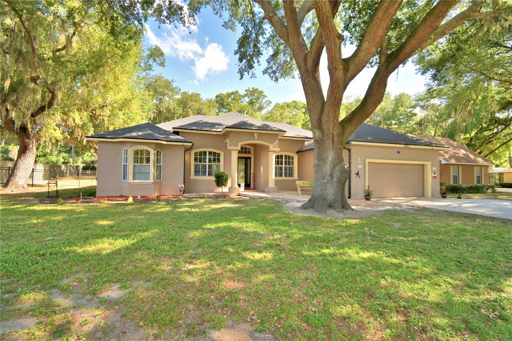 A single-story tan house with a two-car garage sits behind a large oak tree — 1 LAKE ELOISE LANE, WINTER HAVEN, FL