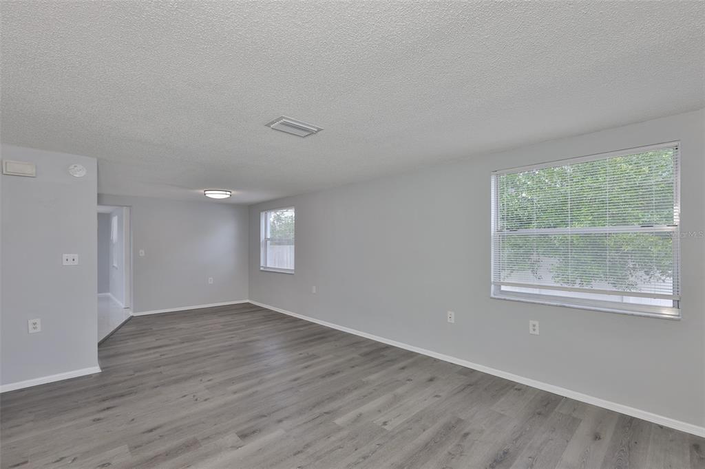 An empty living room features gray walls, wood-look flooring, and two windows with blinds — 5637 GOLDEN NUGGET DRIVE, HOLIDAY, FL