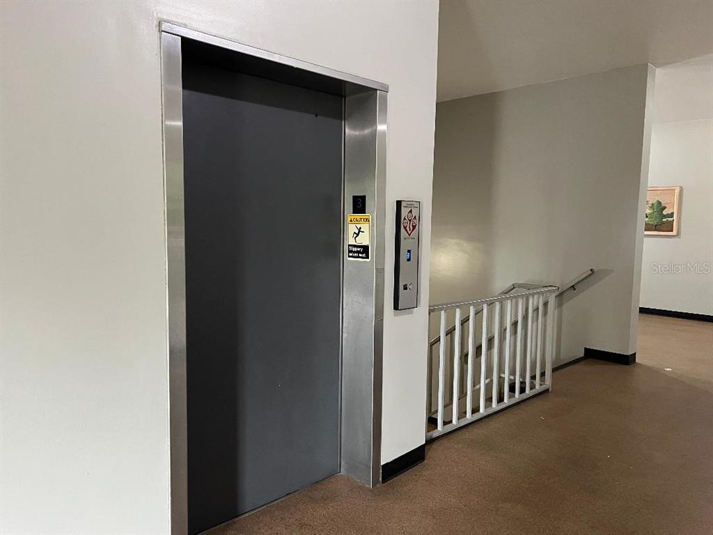 An elevator door and a staircase with a white railing are in a hallway — 2370 JAMAICAN STREET UNIT 74, CLEARWATER, FL