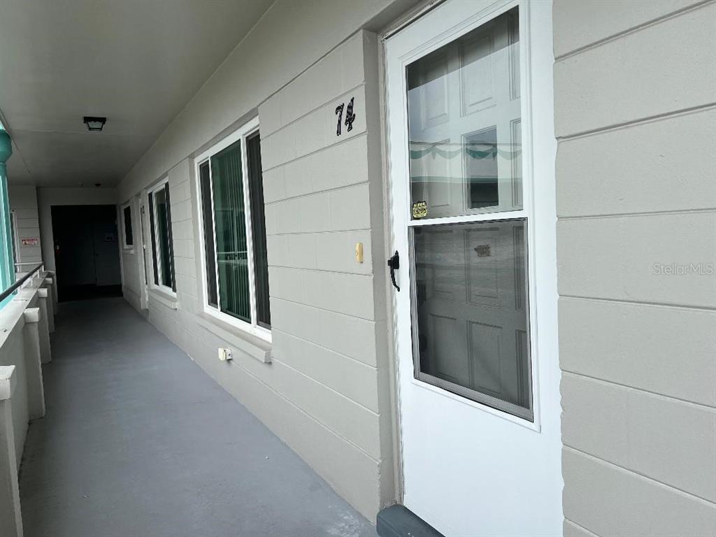 An exterior walkway leads to a gray door marked with the number 74 — 2370 JAMAICAN STREET UNIT 74, CLEARWATER, FL