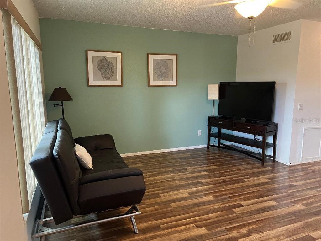 A living room features a black sofa, a television on a stand, and wood flooring — 2370 JAMAICAN STREET UNIT 74, CLEARWATER, FL