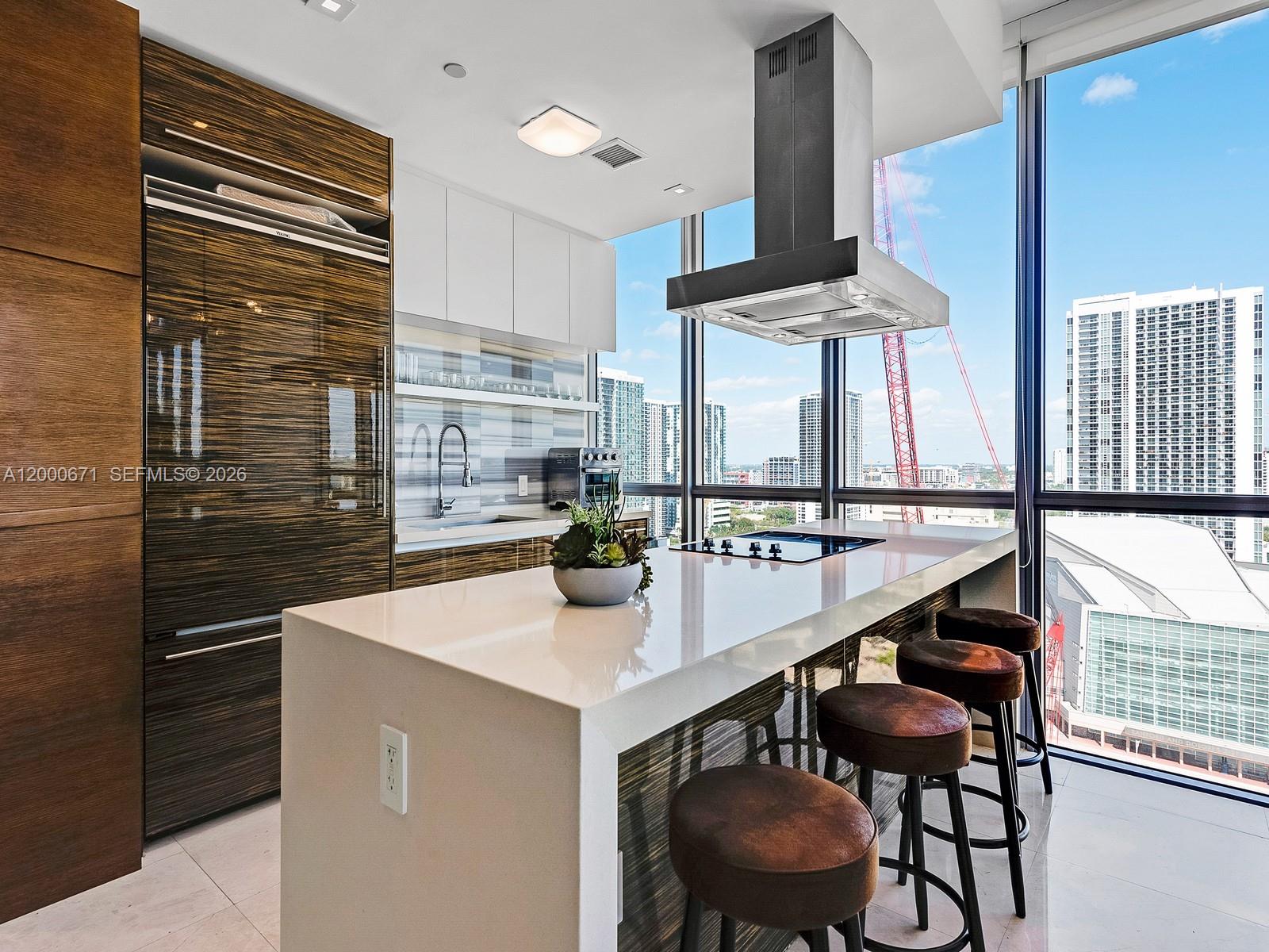 A modern kitchen features a white island with bar stools, wood-grain cabinetry, and floor-to-ceiling windows — 1100 Biscayne Blvd # 2105, Miami FL 33132, MIAMI, FL