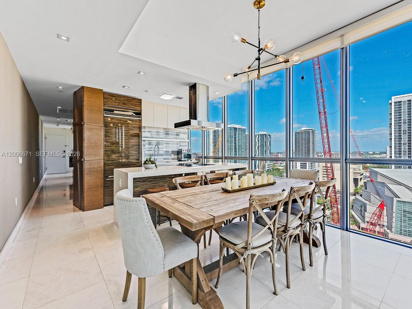 A modern dining area and kitchen feature a wooden table, floor-to-ceiling windows, and city views — 1100 Biscayne Blvd # 2105, Miami FL 33132, MIAMI, FL