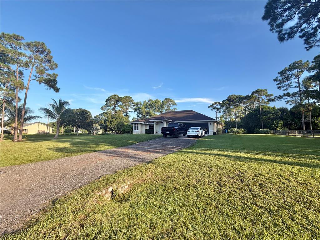 A single-story house with a gravel driveway sits on a large, grassy lot with trees — 17770 64TH PLACE N, LOXAHATCHEE, FL