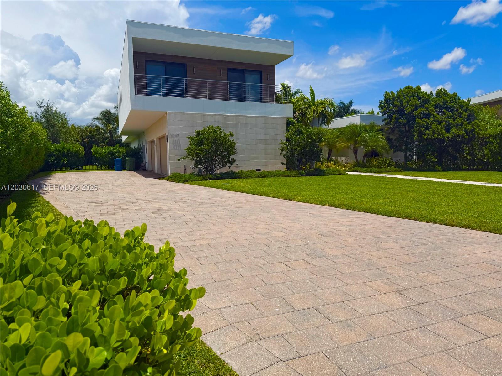 A modern two-story house with a stone facade and a paved driveway under a blue sky — 16569 Botaniko Dr N, Weston FL 33326, WESTON, FL