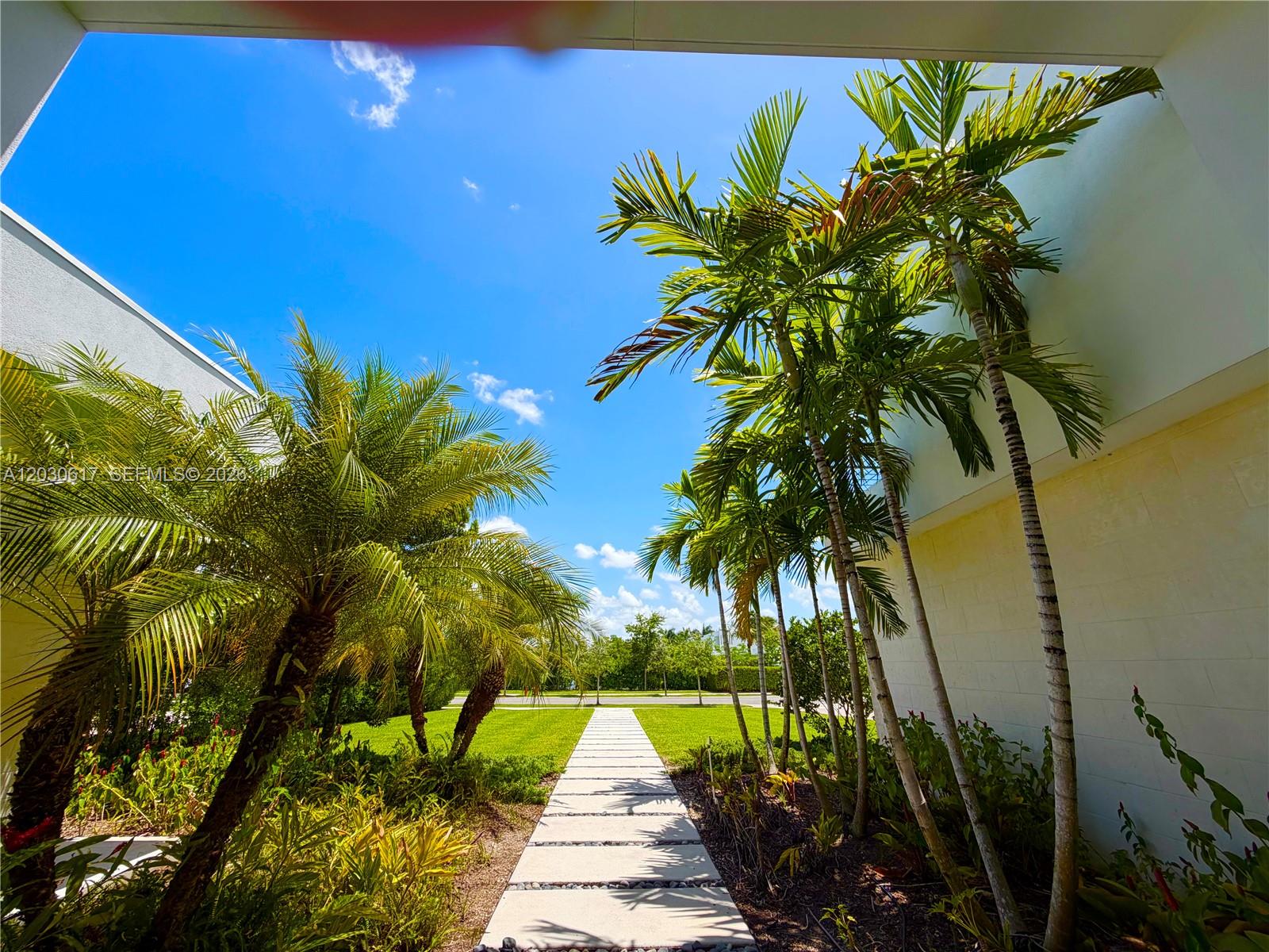 A stone walkway leads through a landscaped yard between two buildings under a blue sky — 16569 Botaniko Dr N, Weston FL 33326, WESTON, FL