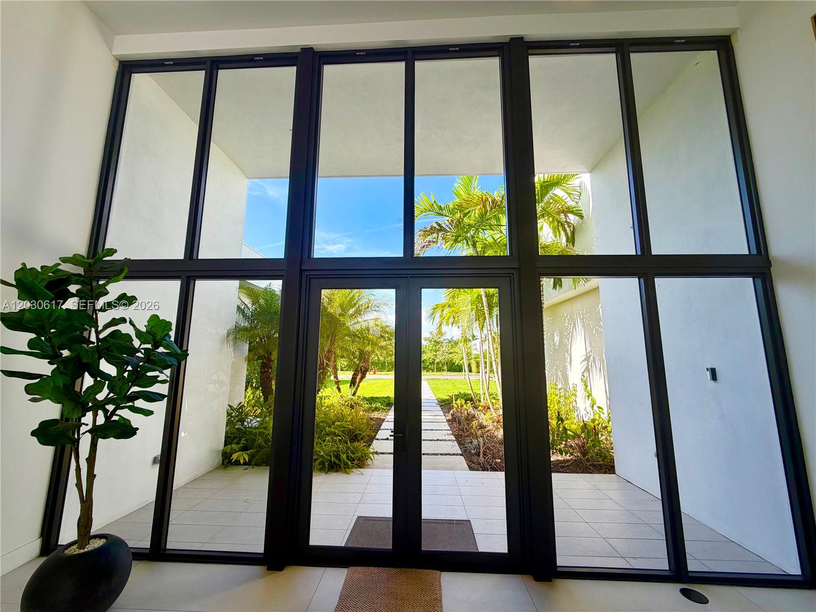 A tall glass entryway features black metal frames, a potted plant, and a view of landscaping — 16569 Botaniko Dr N, Weston FL 33326, WESTON, FL