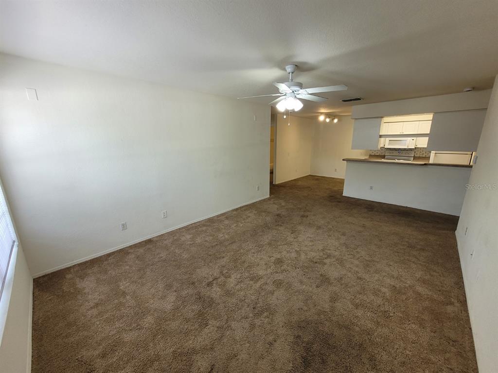 A living room with brown carpet, white walls, a ceiling fan, and an open kitchen — 5914 WILLOW RIDGE DRIVE UNIT 101, ZEPHYRHILLS, FL