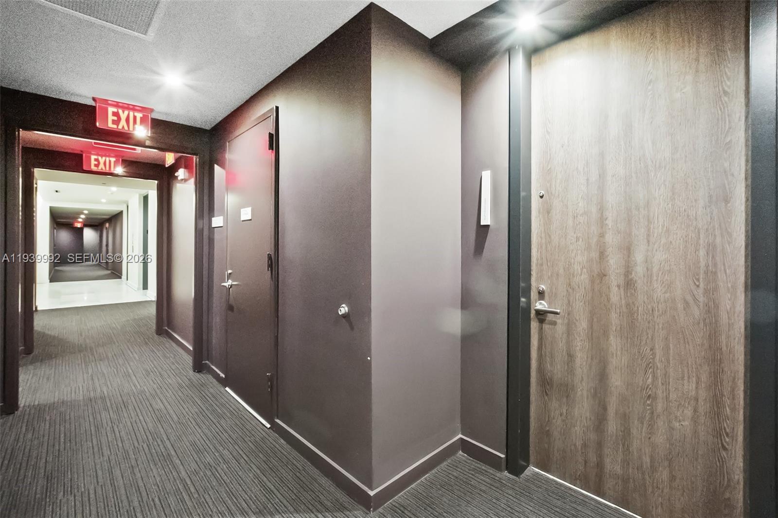 A hallway features dark walls, carpeted flooring, two doors, and illuminated exit signs — 68 SE 6th Street # 805, Miami FL 33131, MIAMI, FL