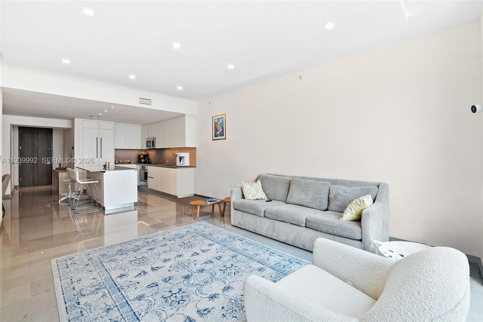 A modern open-concept living room features a gray sofa, a patterned rug, and a kitchen — 68 SE 6th Street # 805, Miami FL 33131, MIAMI, FL