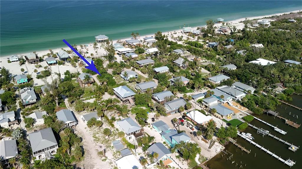An aerial view shows a coastal neighborhood with houses, sandy paths, and boat docks — 8480 LITTLE GASPARILLA ISLAND, PLACIDA, FL