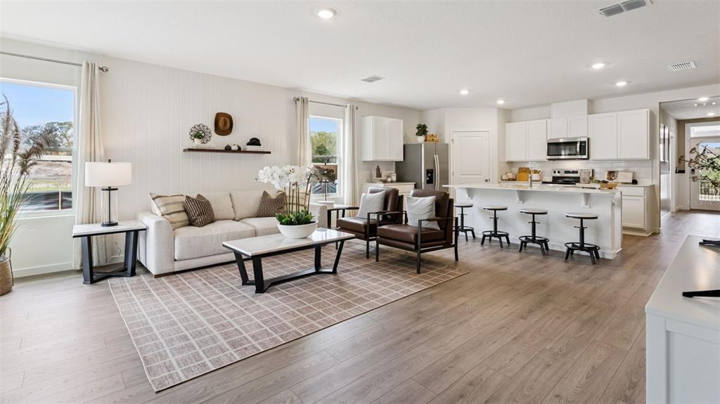 An open-concept living room and kitchen feature white cabinetry, wood-look flooring, and neutral furniture — 3103 HOUSE FINCH ROAD, ST CLOUD, FL