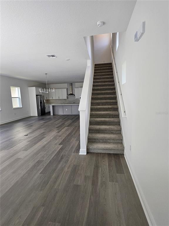 An open-concept living area features wood-look flooring, a kitchen, and a carpeted staircase — 10172 PEARSON AVENUE, ORLANDO, FL